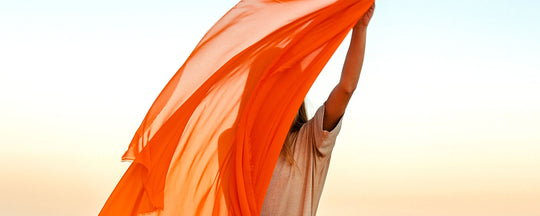 A woman holding an orange scarf to her face, symbolizing freshness and vitality. Her skin appears radiant and healthy, reflecting the theme of skincare and wellness.