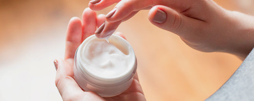 Woman dipping her hand into a jar of moisturizer, showcasing the rich, creamy texture of a spring skincare product.