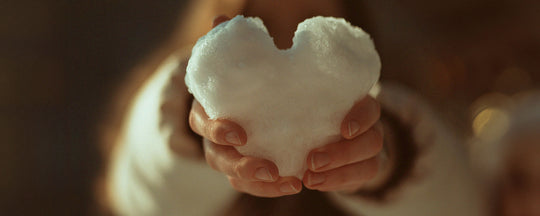 An image of a woman cradling a delicately crafted heart made of snow in her hands, symbolizing the care and tenderness required in nurturing sensitive skin during the harsh winter months.