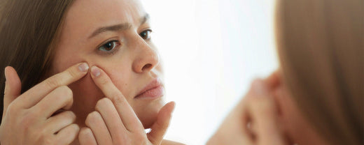 Woman examining and picking at her skin in front of a mirror, highlighting concerns over skin health and the importance of a proper skincare routine.