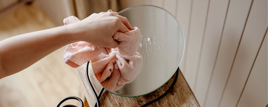 A hand holding a cloth, gently wiping a mirror to reveal a clean, reflective surface.
