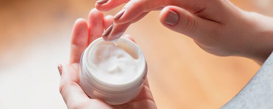 Woman dipping her hand into a jar of moisturizer, showcasing the rich, creamy texture of a spring skincare product.