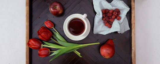 Image of an assortment of red fruits, including strawberries and raspberries, next to a cup of red tea, arranged aesthetically to highlight their vibrant colors and freshness, emphasizing a healthy, antioxidant-rich diet.