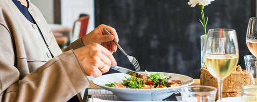 Person sitting at a table enjoying a healthy meal of salad and fruit juice, representing a diet beneficial for skin health.