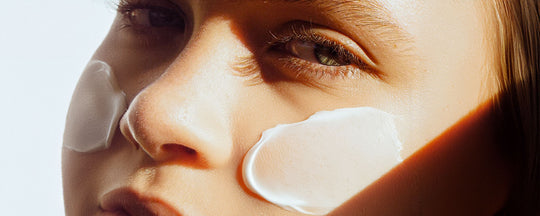 Woman with creams applied to both cheeks, demonstrating a skincare routine.