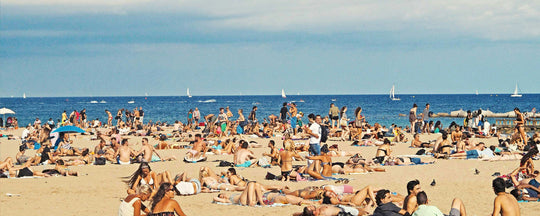 Crowded beach scene showing numerous people sunbathing and enjoying the sunny day.