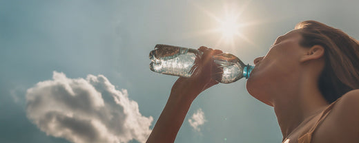 A woman drinking water from a plastic bottle under the bright sun, symbolizing the importance of hydration and sun protection as part of an effective anti-aging skincare routine.