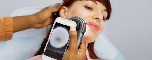 Close-up of a dermatologist examining a patient's skin with a handheld dermatoscope connected to a smartphone, showcasing professional skincare analysis.