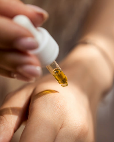 Close-up of a hand applying serum from a dropper to another hand, demonstrating the precise application of a targeted skincare treatment for enhanced skin nourishment and health.