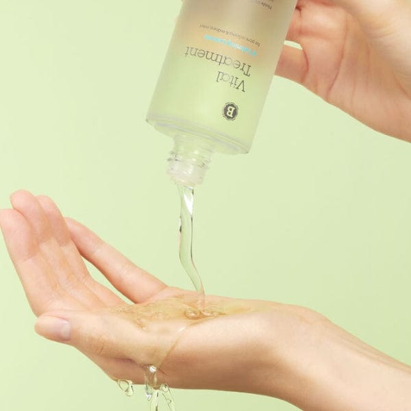Vital Treatment liquid pouring on hand against a green background