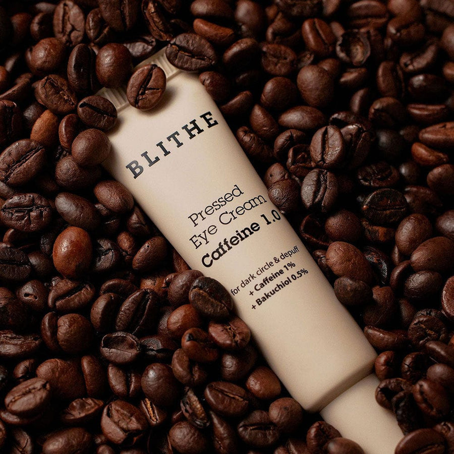Pressed Eye Cream Caffeine 1.0 surrounded by coffee beans, showing benefits for dark circles and puffiness reduction