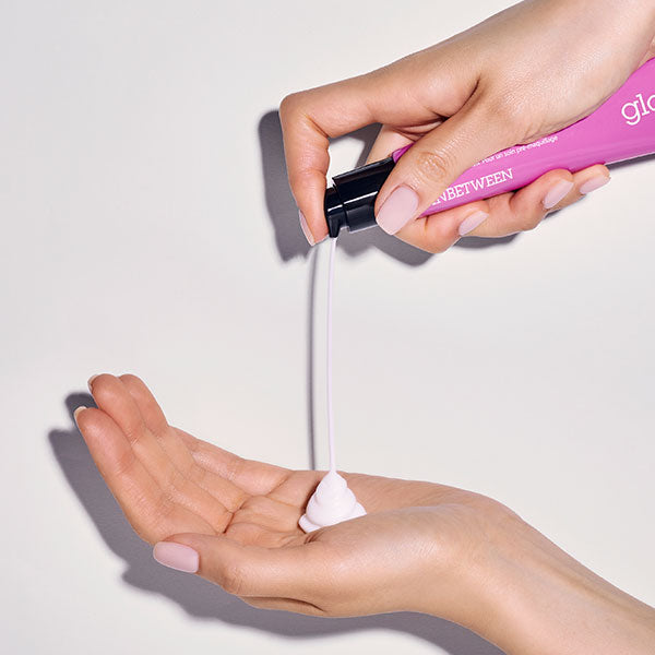a woman dispensing Inbetween Glow Primer into her hand from a pink bottle