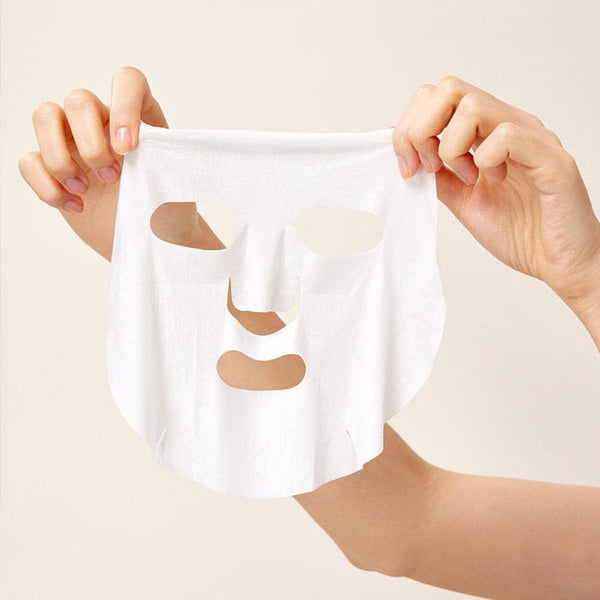 a person holding up a white facial sheet mask against a beige background